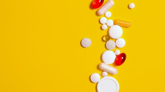 A selection of different pills on a yellow background.