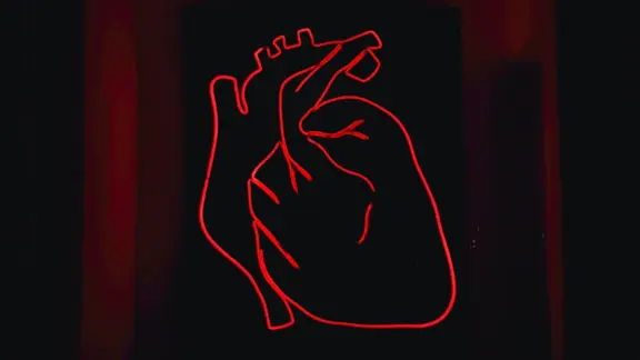 A red light LED model of the heart mounted on a black surface.