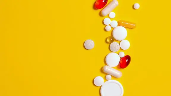 A selection of different pills on a yellow background.