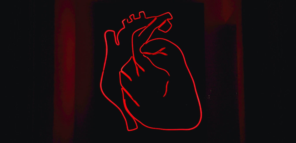 A red light LED model of the heart mounted on a black surface.
