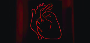 A red light LED model of the heart mounted on a black surface.