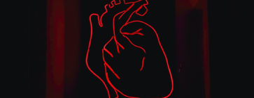 A red light LED model of the heart mounted on a black surface.