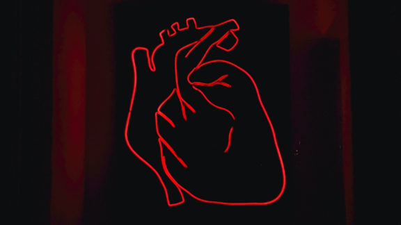 A red light LED model of the heart mounted on a black surface.