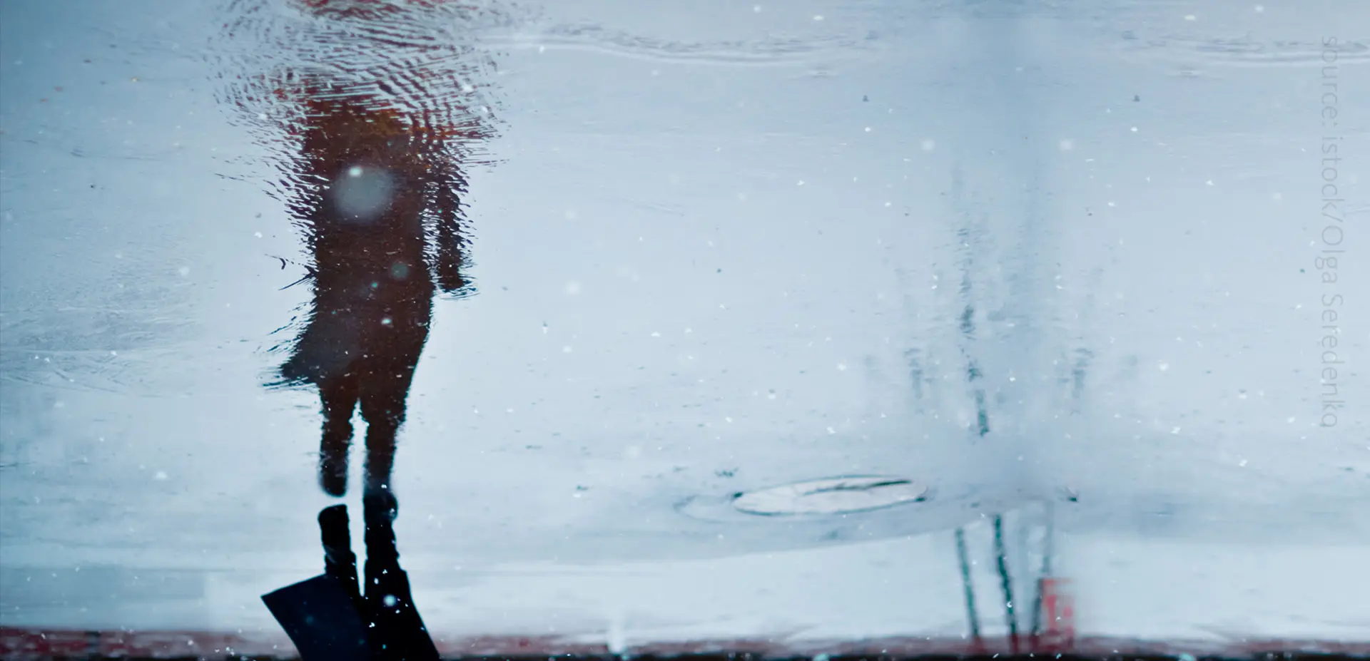 A photo of a person mirrored by a puddle.