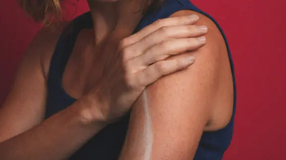 A photo of a person applying a cream on their shoulder.