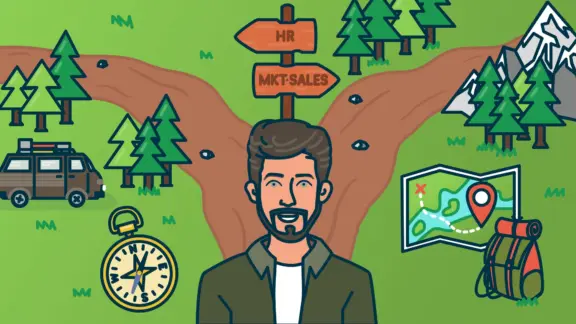 A man wearing a green shirt in the middle of two paths in the mountains.